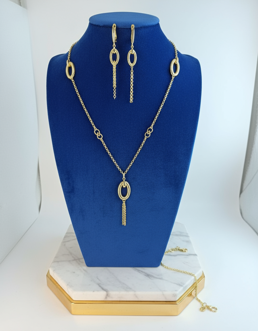 Gold necklace and earrings set on a blue velvet stand with a white background