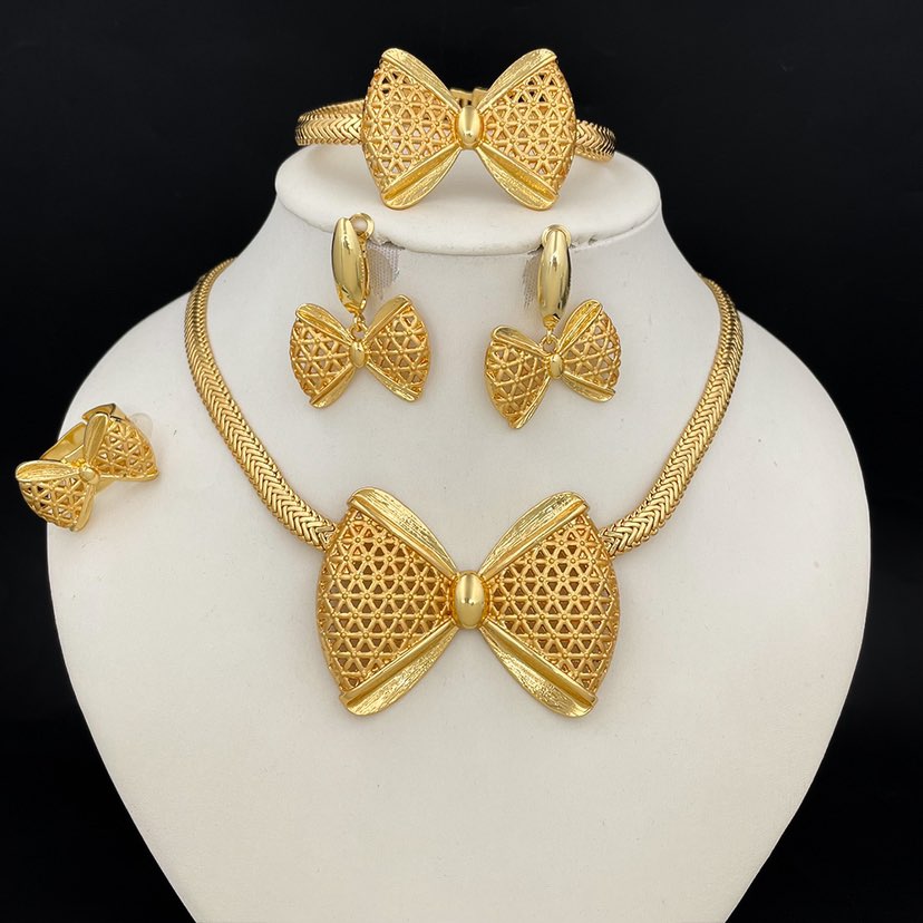 Gold bow-shaped jewelry set on a white stand with a black background