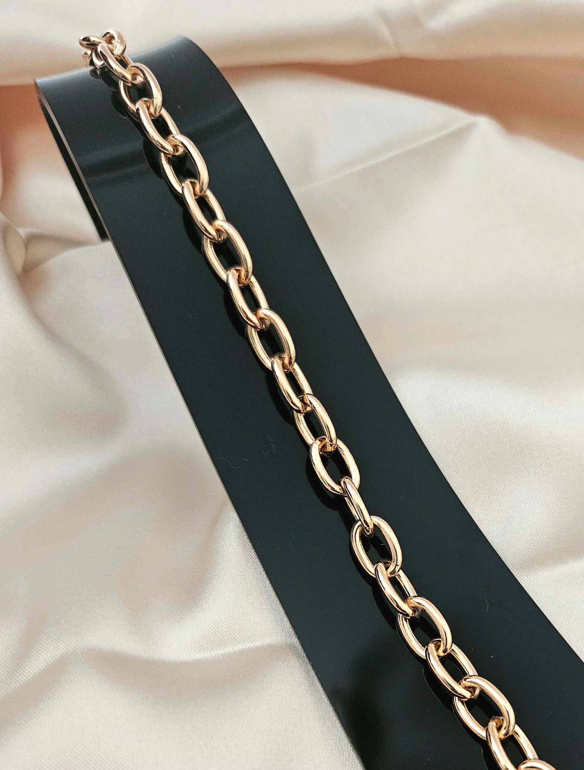 Gold chain on a black belt against a beige fabric background