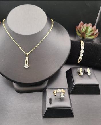Gold jewelry set including necklace, bracelet, ring, and earrings on black stands.