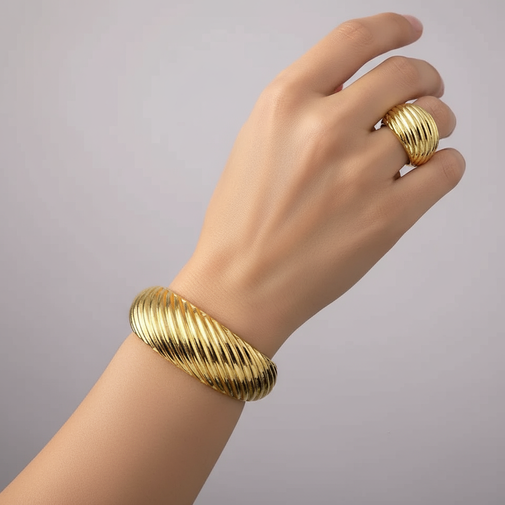 Gold bracelet and ring on a mannequin hand against a gray background
