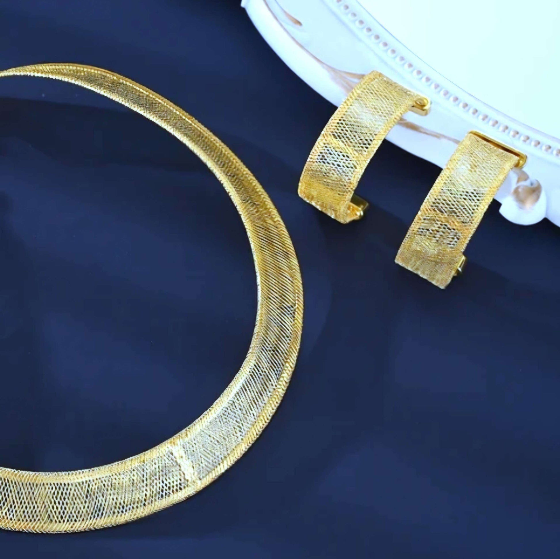 Gold necklace and bracelet set on a dark blue fabric background