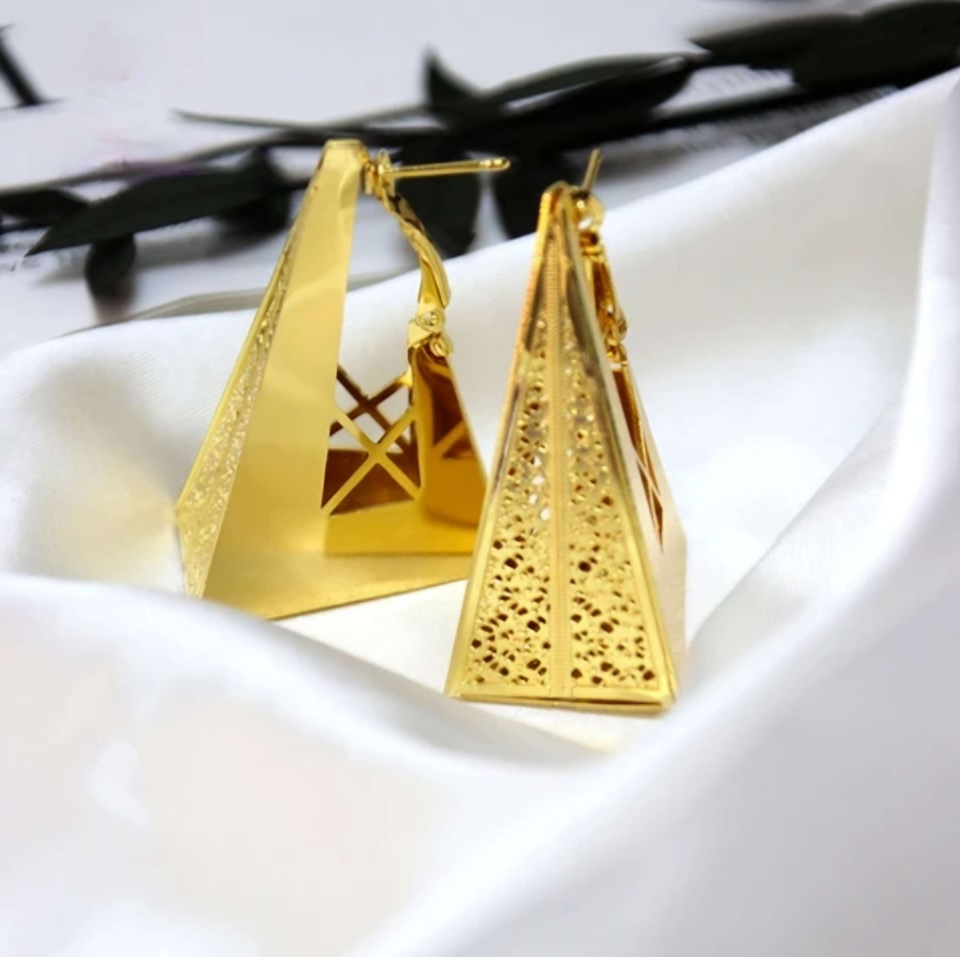 Gold pyramid-shaped earrings on a white surface with a pen in the background