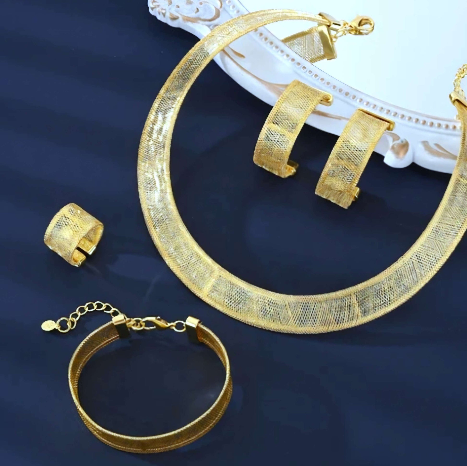 Gold jewelry set including necklace, bracelet, and earrings on a dark blue background