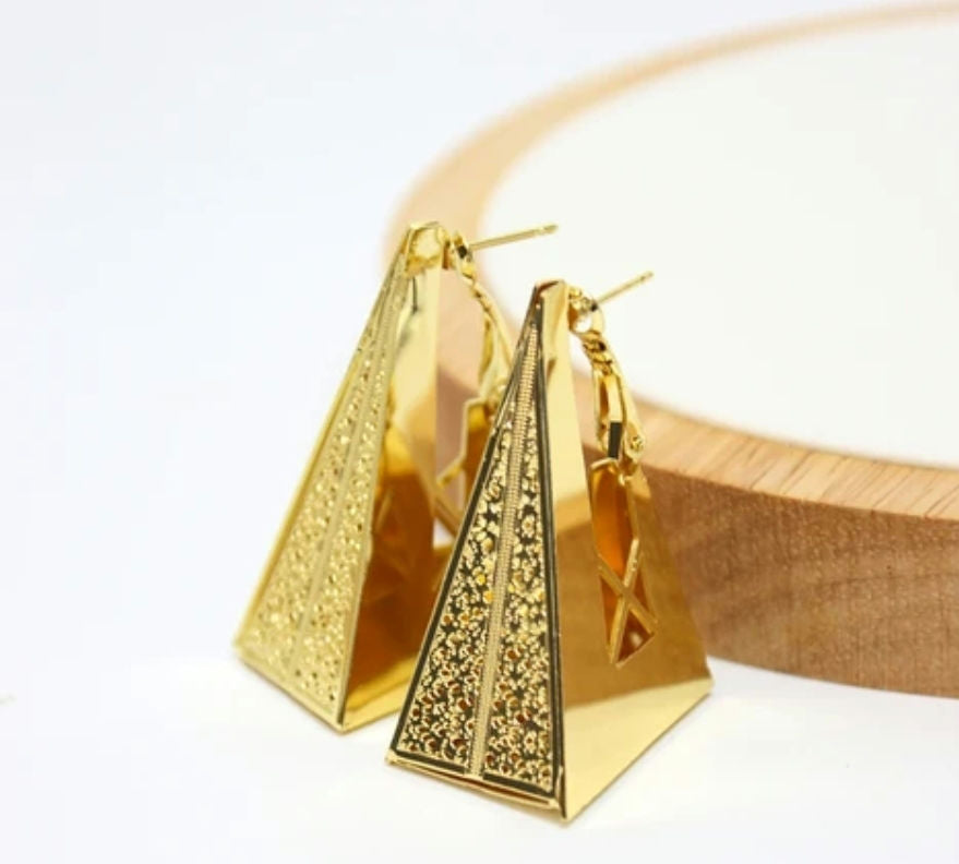 Gold pyramid-shaped earrings on a white surface with a wooden box in the background.