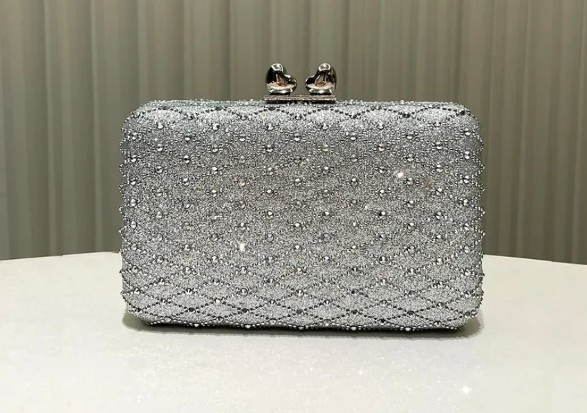 Silver beaded clutch bag on a white surface with a neutral background