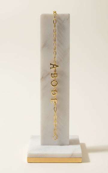 Gold necklace with letter pendants on a marble stand against a white background