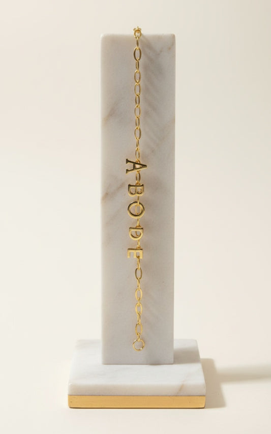 Gold necklace with letter pendants on a marble stand against a white background