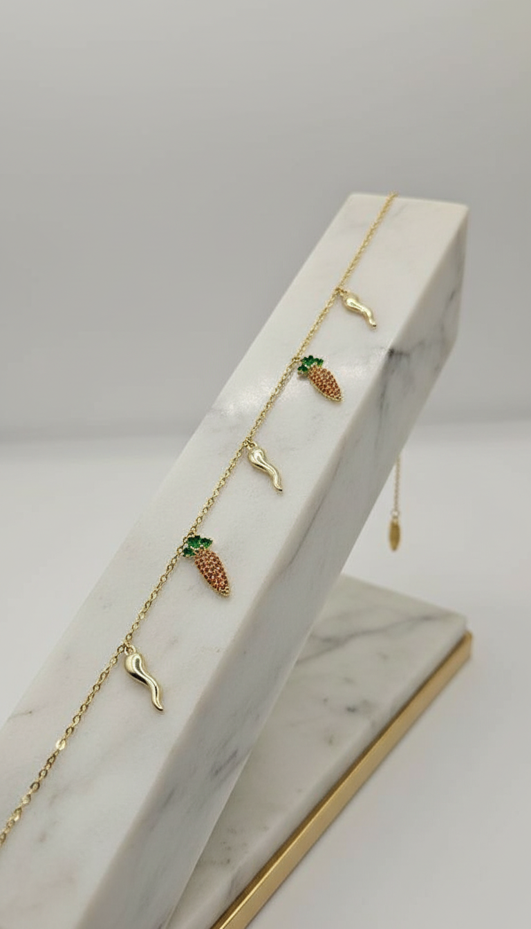 Gold necklace with pineapple and leaf pendants on a marble stand.