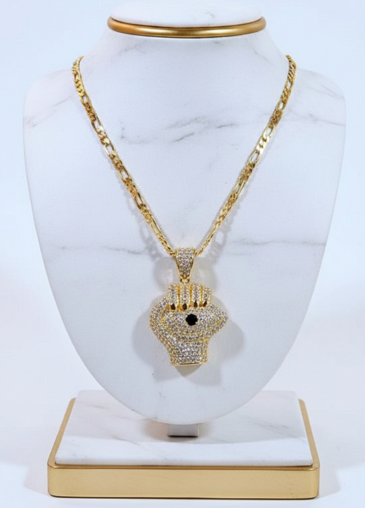 Gold necklace with a fist shaped pendant on a white marble stand.