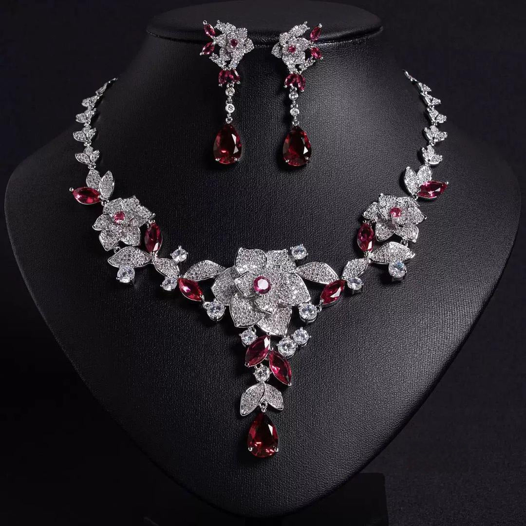 Cubic zirconia Jewelry set with necklace and earrings featuring red and clear gemstones on a black stand.