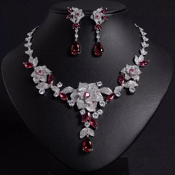 Cubic zirconia Jewelry set with necklace and earrings featuring red and clear gemstones on a black stand.