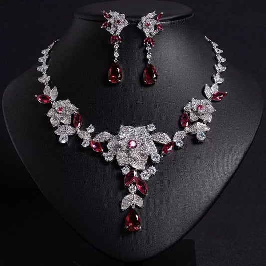 Cubic zirconia Jewelry set with necklace and earrings featuring red and clear gemstones on a black stand.