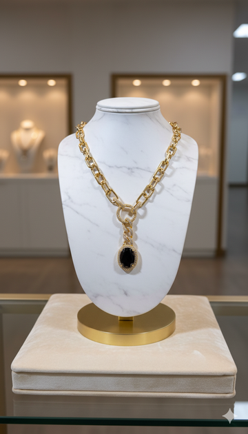 Gold chain necklace with a black pendant on a marble bust in a jewelry store setting.