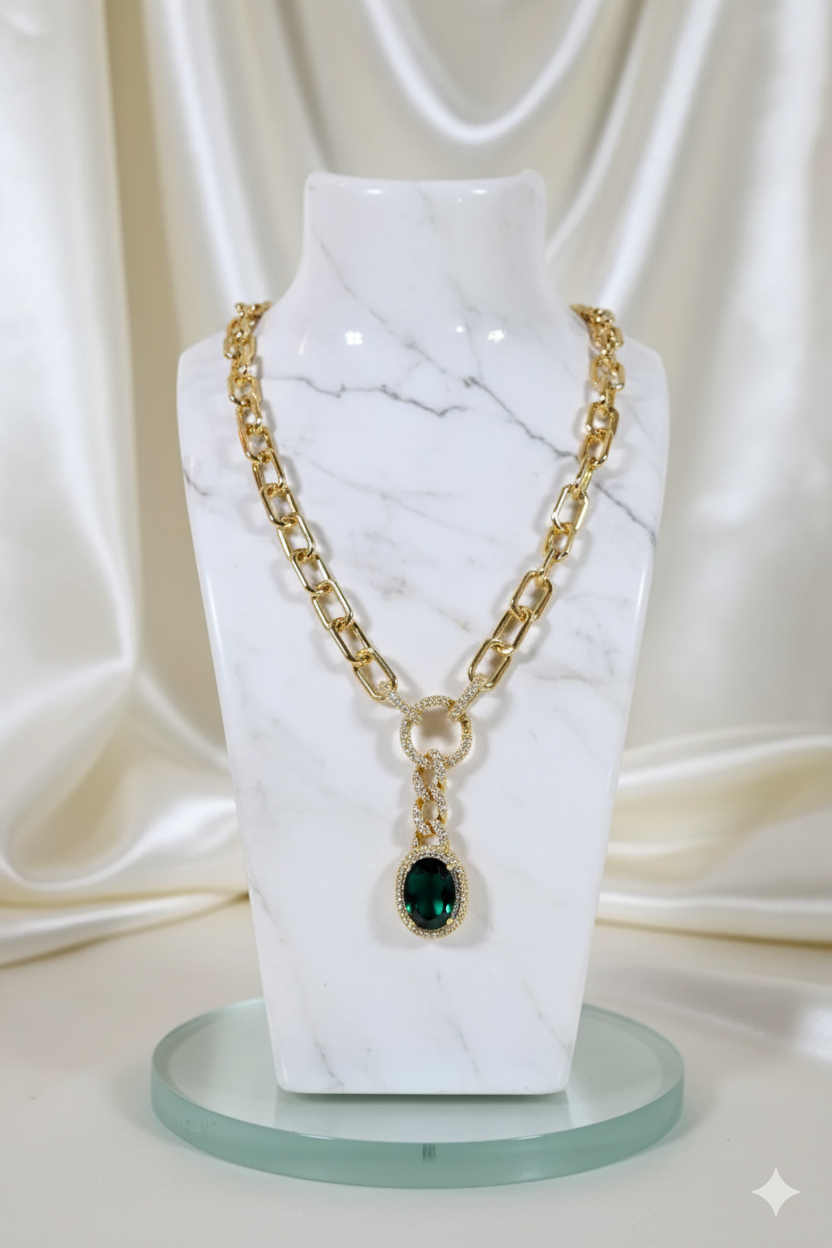 Gold chain necklace with a green pendant on a marble stand against a white curtain background