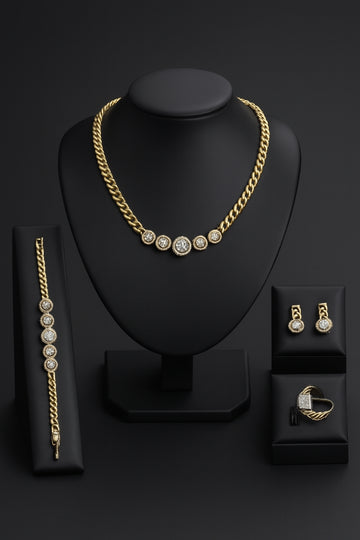 Gold jewelry set including necklace, bracelet, and earrings on a black stand with a black background.