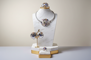 Jewelry set including necklace, earrings, and ring on a marble stand with a beige background