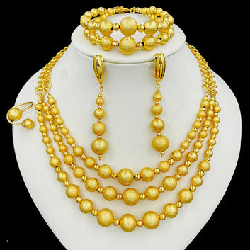 Gold jewelry set including necklace, bracelet, and earrings on a white stand.