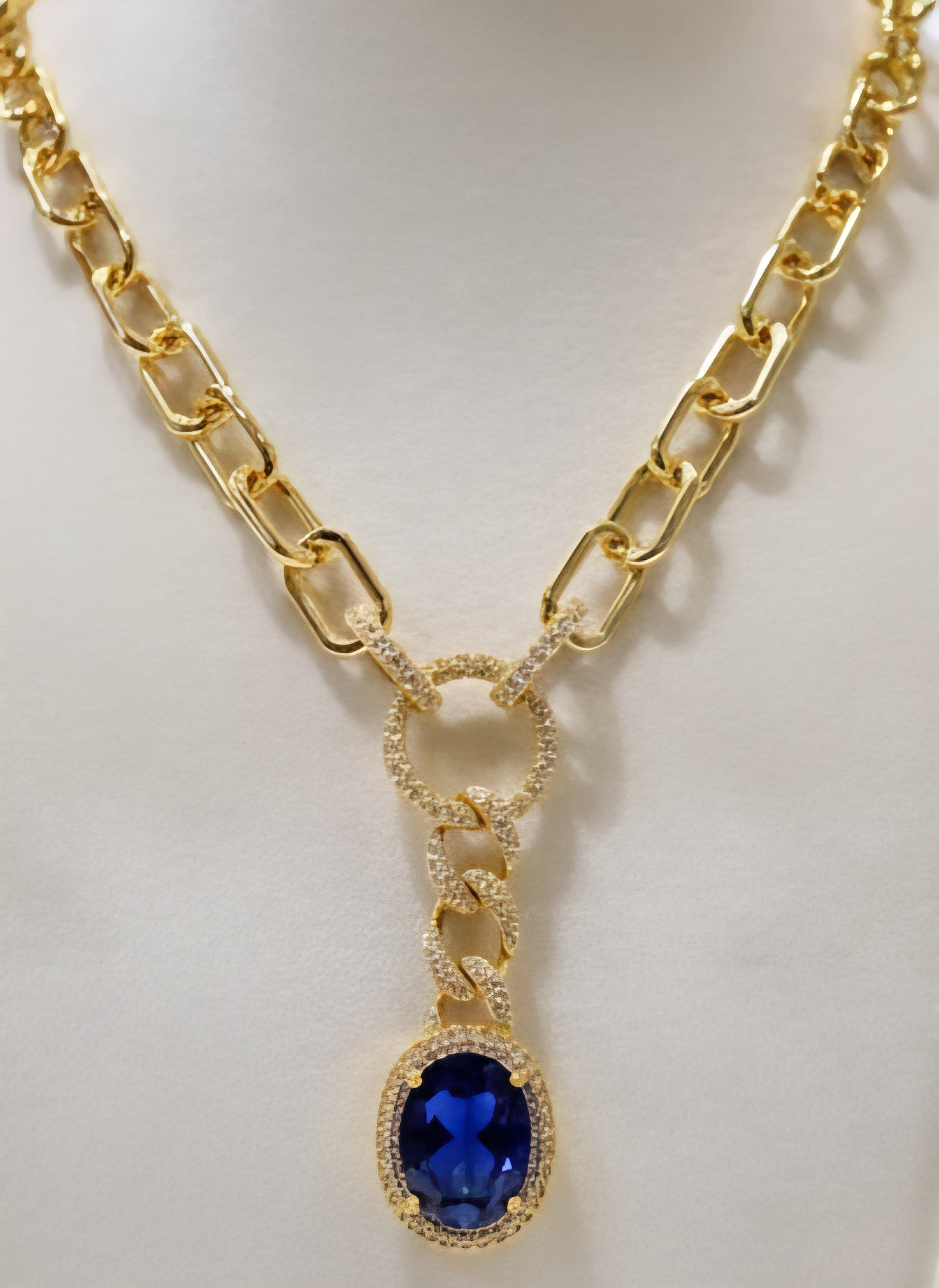Gold necklace with a blue gemstone pendant on a white background