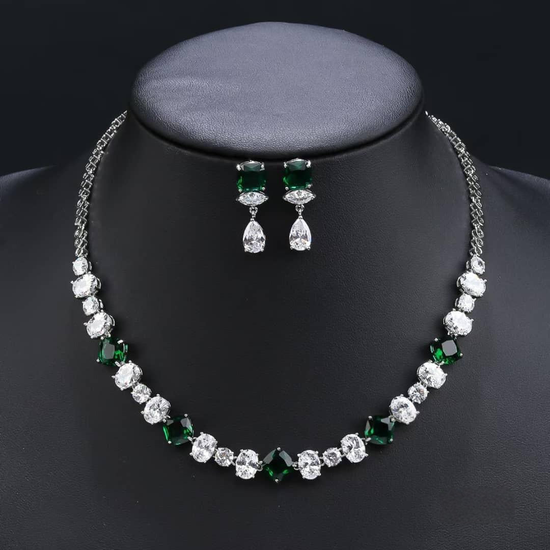 Necklace and earrings set with green and clear stones on a black mannequin.