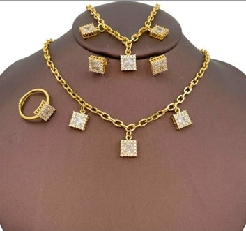 A 4-piece gold-plated jewelry set displayed on a brown mannequin bust, featuring a matching necklace, link bracelet, stud earrings, and an adjustable ring, all adorned with square-cut crystal charms surrounded by a pavé border.