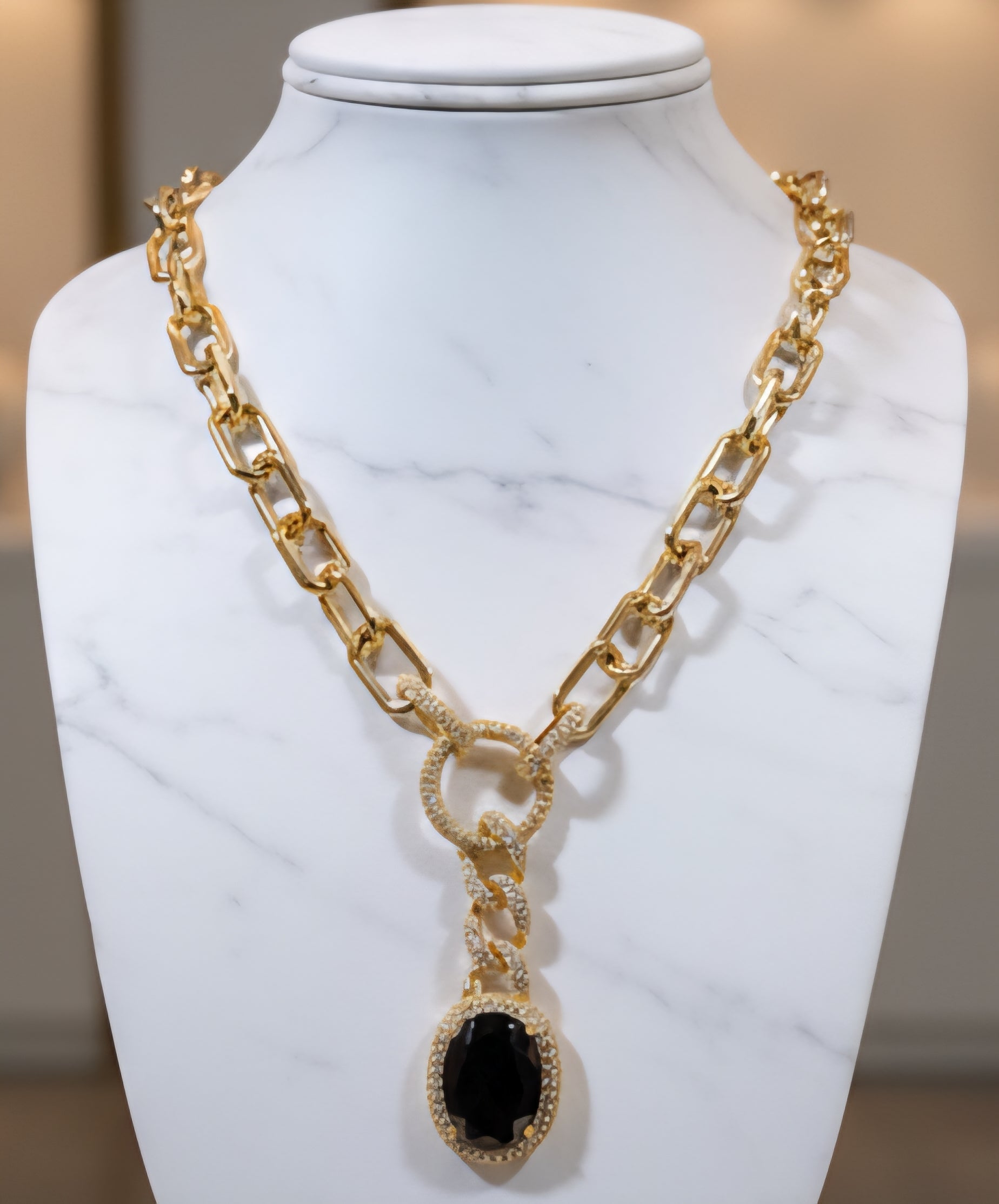 Gold chain necklace with a black pendant on a marble stand