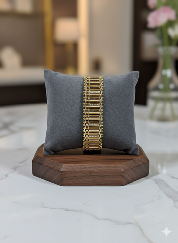Gold bracelet on a gray pillow with a wooden base, blurred indoor background