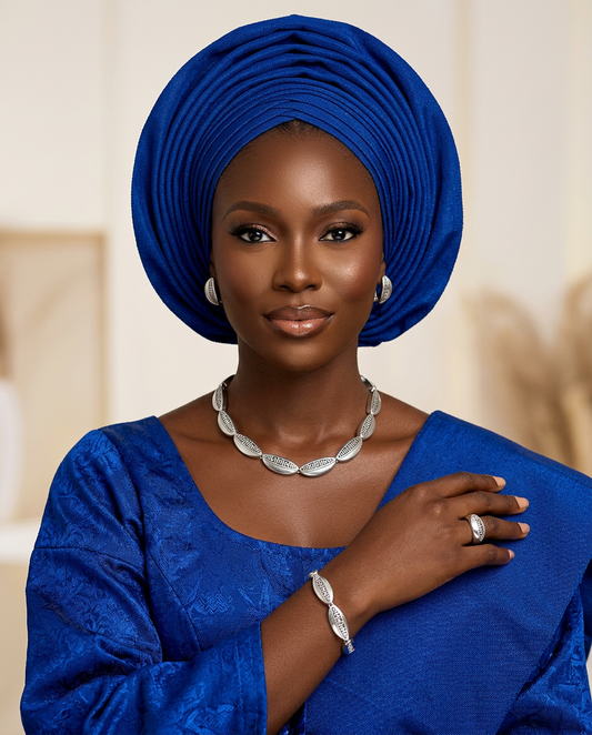 Woman wearing a blue traditional outfit with a matching headwrap, jewelry, and a neutral background.