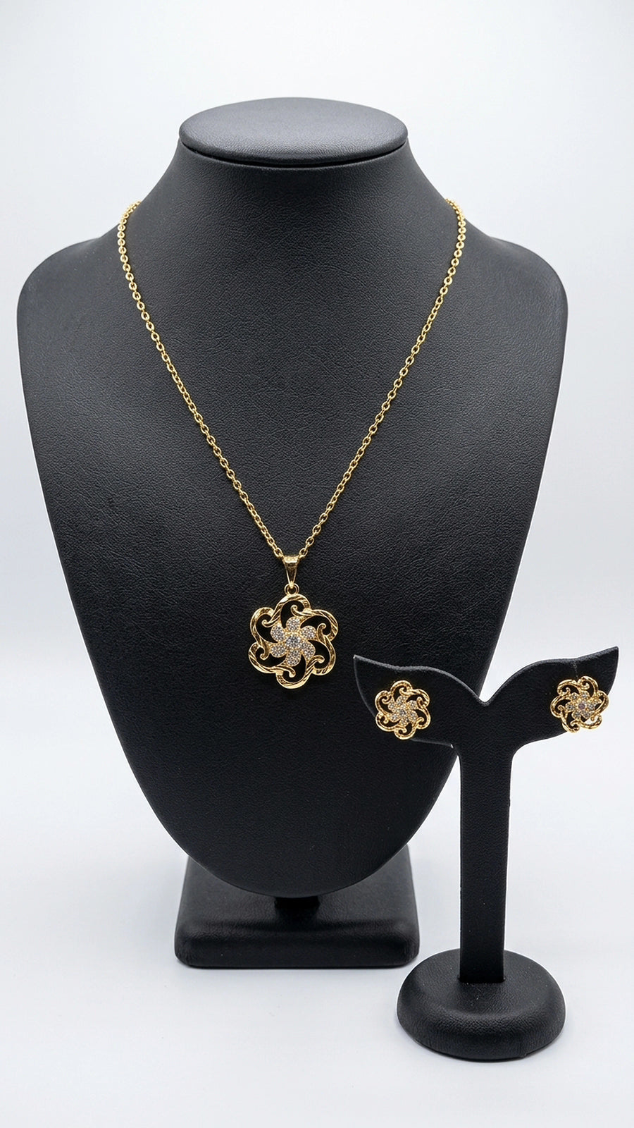 Gold necklace and earrings on a black mannequin bust with a white background