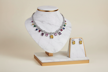 Jewelry set with a necklace and earrings on a white marble stand with gold accents.